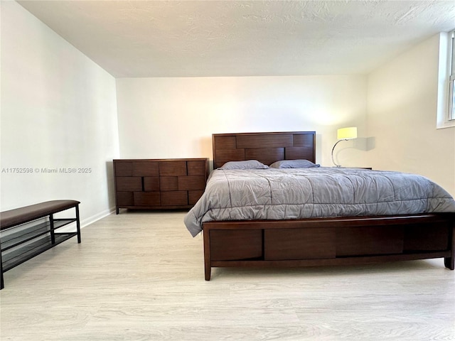 bedroom featuring light wood-type flooring, a textured ceiling, and baseboards