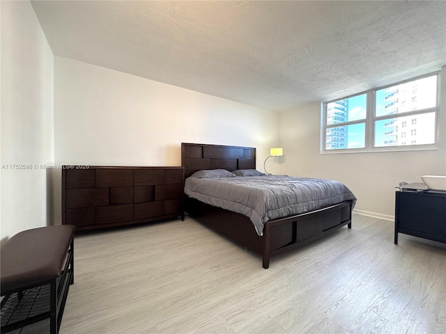 bedroom featuring light wood-type flooring, a textured ceiling, and baseboards