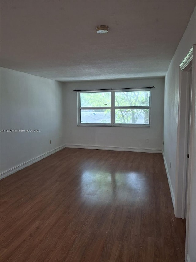 spare room featuring dark wood-style flooring and baseboards