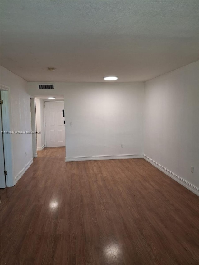 unfurnished room featuring dark wood-style flooring, visible vents, a textured ceiling, and baseboards