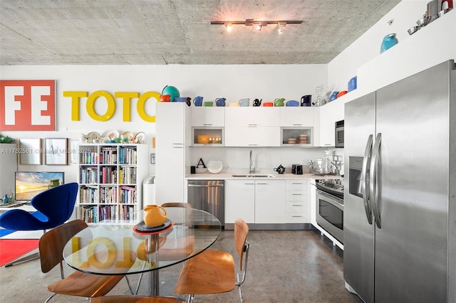 kitchen featuring stainless steel appliances, light countertops, white cabinetry, a sink, and concrete floors