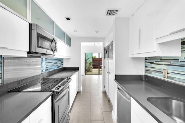 kitchen featuring glass insert cabinets, dark countertops, white cabinetry, and appliances with stainless steel finishes