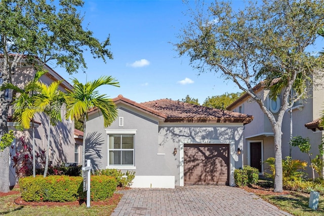 mediterranean / spanish house featuring a garage, a tile roof, decorative driveway, and stucco siding