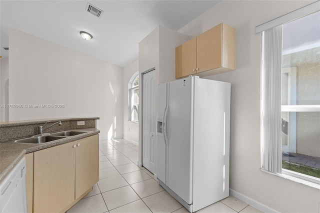 kitchen featuring white appliances, light tile patterned floors, visible vents, light brown cabinetry, and a sink