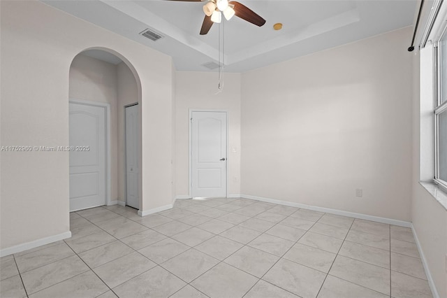 empty room with arched walkways, a tray ceiling, visible vents, and baseboards