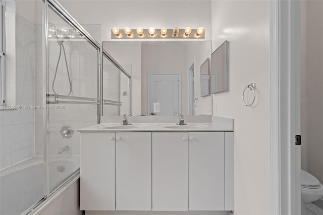 bathroom featuring double vanity, shower / bath combination with glass door, a sink, and toilet