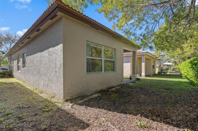 view of side of home with a yard, a tile roof, and stucco siding