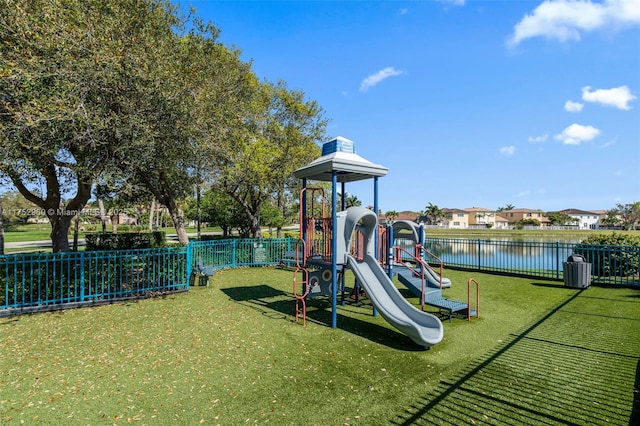 communal playground with a water view, fence, and a lawn