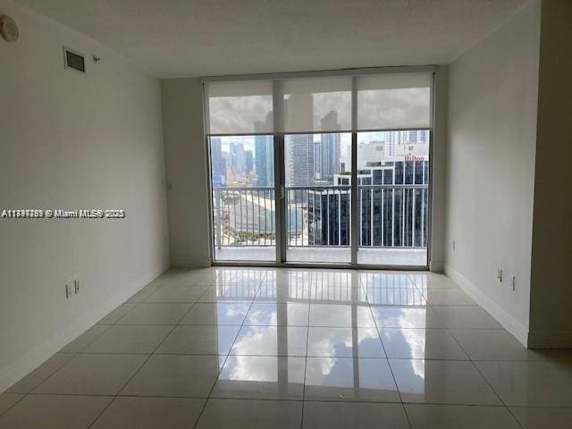 spare room featuring light tile patterned floors, visible vents, baseboards, and a wall of windows