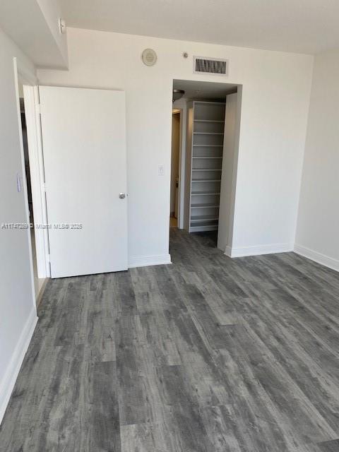 spare room featuring dark wood-type flooring, visible vents, and baseboards