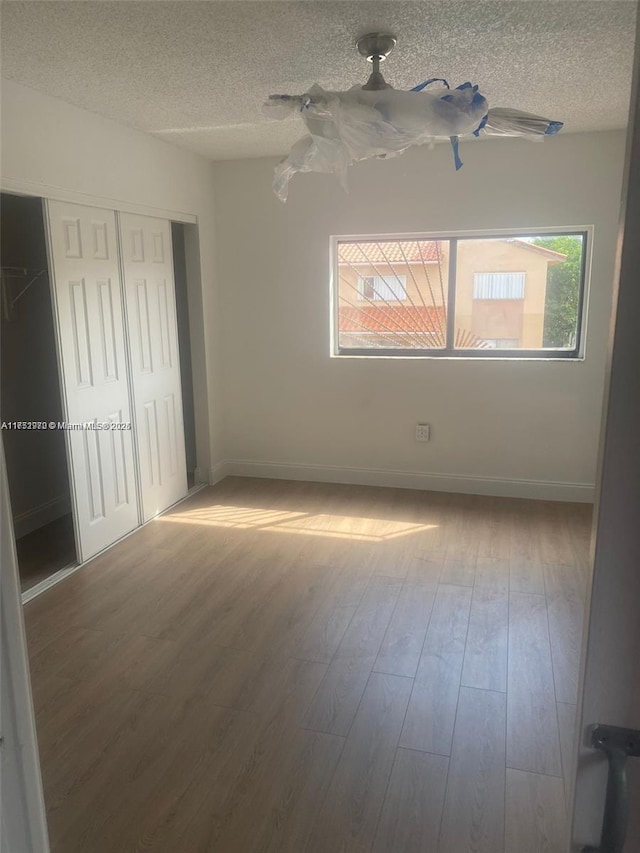 unfurnished bedroom with a textured ceiling, a closet, wood finished floors, and baseboards