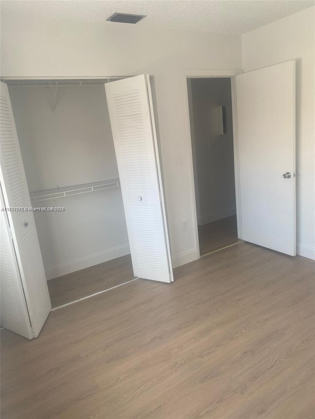 unfurnished bedroom with a closet, baseboards, light wood-style flooring, and a textured ceiling