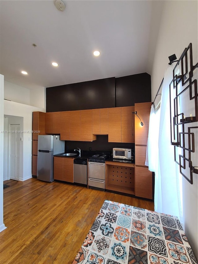 kitchen featuring brown cabinetry, dark countertops, stainless steel appliances, light wood-style floors, and a sink