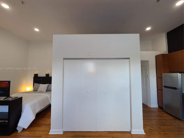 bedroom with a closet, wood finished floors, freestanding refrigerator, and recessed lighting