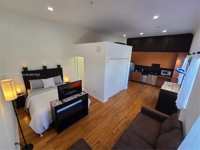 bedroom with light wood-style floors, freestanding refrigerator, visible vents, and recessed lighting