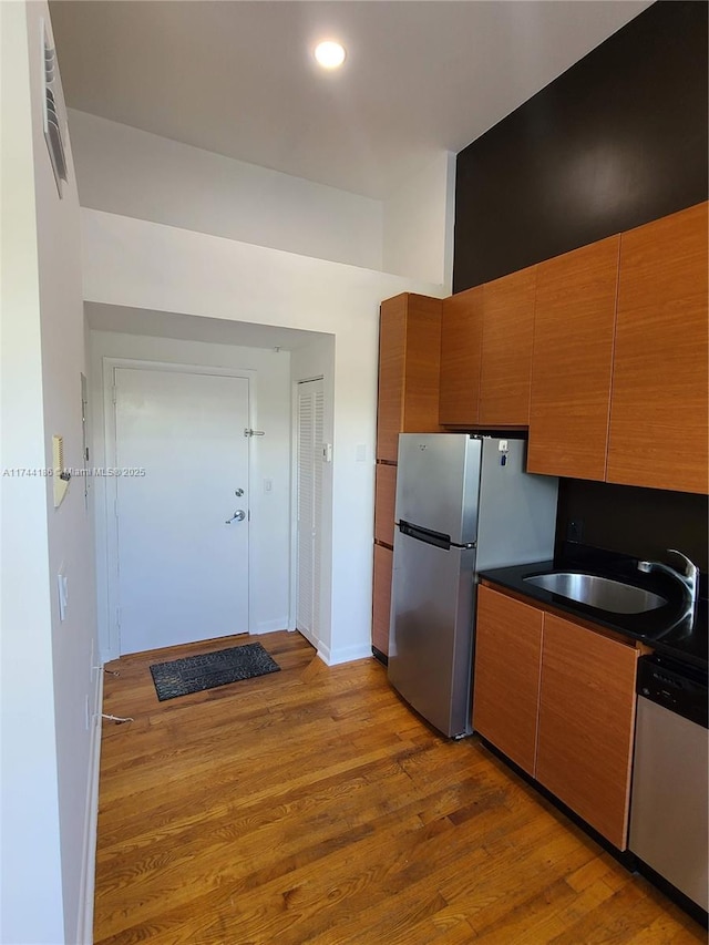 kitchen featuring dark countertops, appliances with stainless steel finishes, brown cabinetry, a sink, and light wood-type flooring