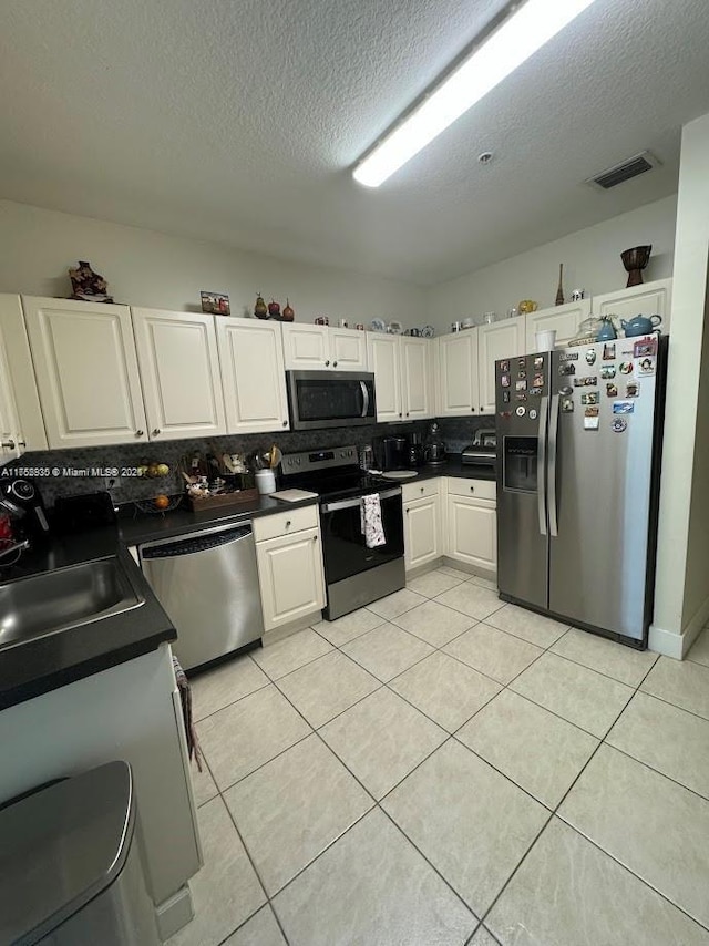 kitchen featuring light tile patterned floors, visible vents, dark countertops, stainless steel appliances, and white cabinetry