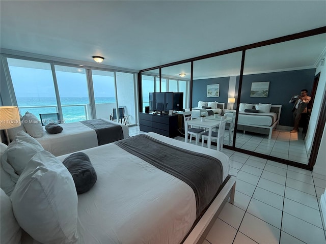 bedroom featuring light tile patterned floors, a water view, and floor to ceiling windows