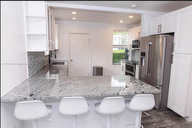 kitchen with a breakfast bar, high end fridge, white cabinetry, a sink, and a peninsula