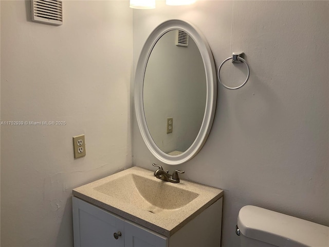 half bathroom with toilet, vanity, and visible vents