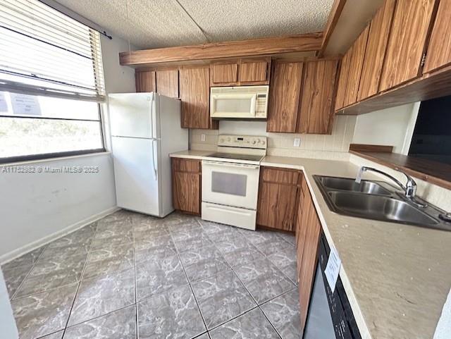 kitchen with white appliances, a sink, light countertops, backsplash, and brown cabinets