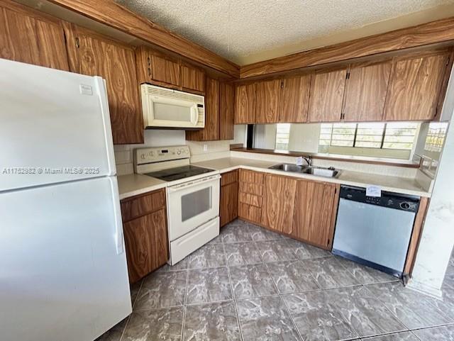 kitchen featuring light countertops, white appliances, brown cabinetry, and a sink