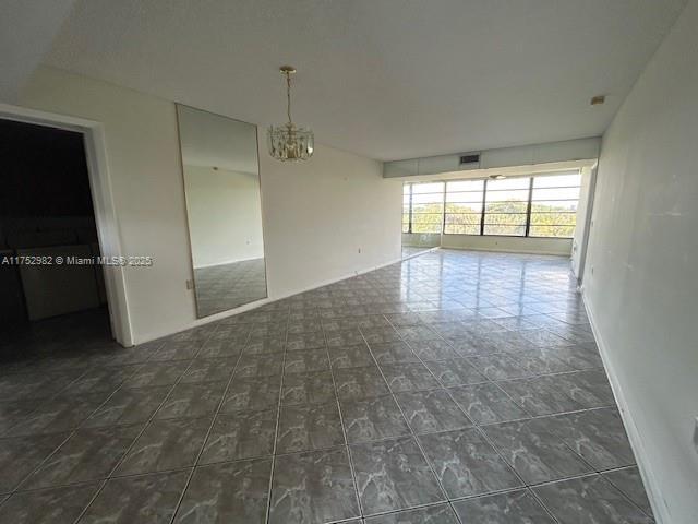 unfurnished room with baseboards, visible vents, and an inviting chandelier