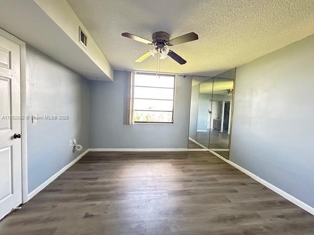 interior space with a textured ceiling, dark wood-style floors, visible vents, and baseboards