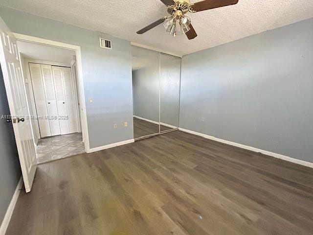 unfurnished bedroom featuring baseboards, visible vents, a ceiling fan, dark wood-style flooring, and a textured ceiling