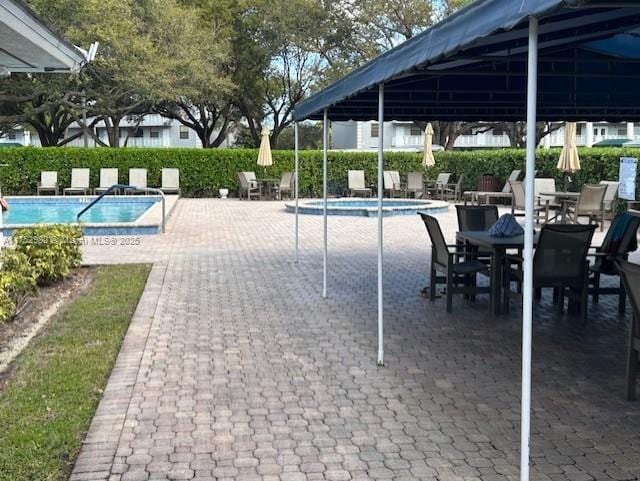 community pool with a patio, a hot tub, and fence