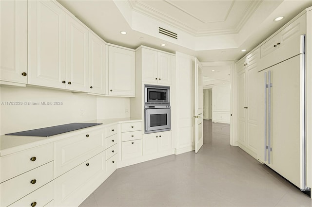 kitchen featuring a tray ceiling, crown molding, recessed lighting, white cabinetry, and built in appliances