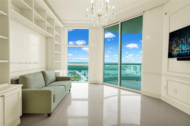 living room featuring built in features, crown molding, a wall of windows, a chandelier, and baseboards