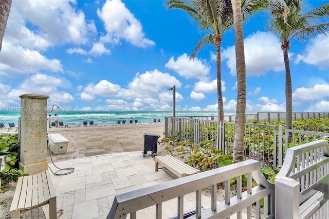 view of patio / terrace with a water view, fence, and a view of the beach