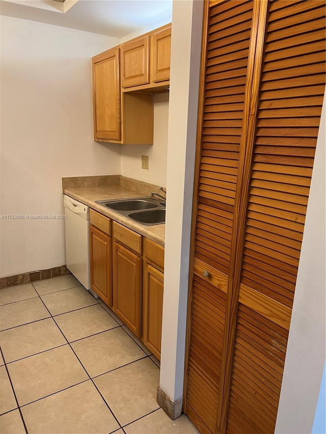 kitchen featuring light tile patterned floors, light countertops, white dishwasher, a sink, and baseboards