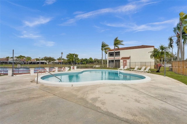 community pool featuring a water view, fence, and a patio