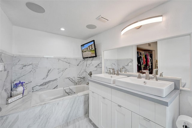 bathroom with visible vents, a sink, a spacious closet, and a garden tub