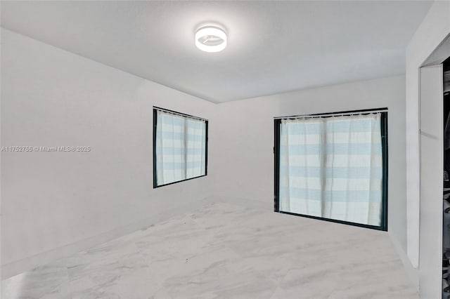 unfurnished room with marble finish floor and baseboards