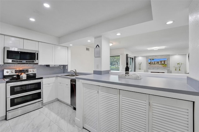 kitchen featuring appliances with stainless steel finishes, white cabinets, a sink, and recessed lighting