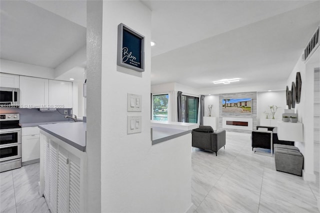 kitchen featuring white cabinets, open floor plan, stainless steel appliances, light countertops, and a fireplace