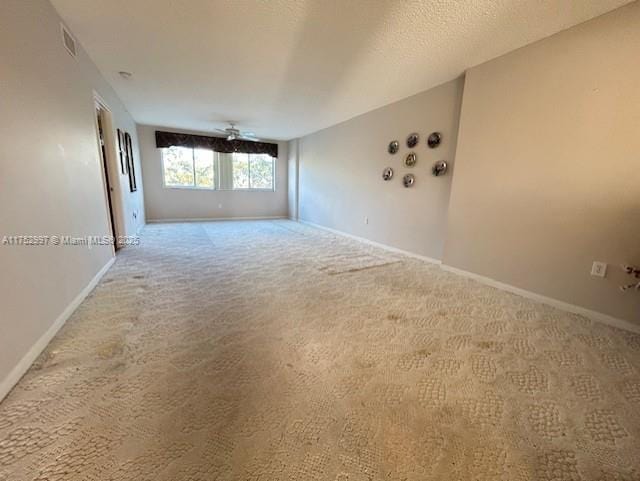 carpeted spare room with a ceiling fan, visible vents, a textured ceiling, and baseboards