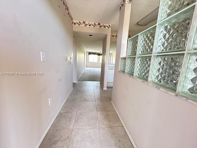 hall featuring baseboards, a textured ceiling, and tile patterned flooring