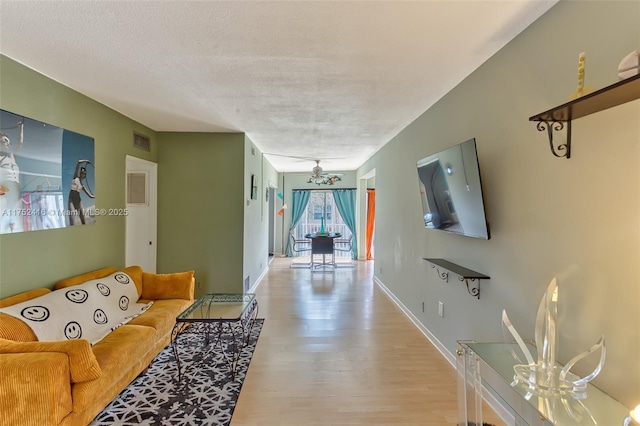 living room featuring light wood-type flooring, baseboards, visible vents, and a textured ceiling