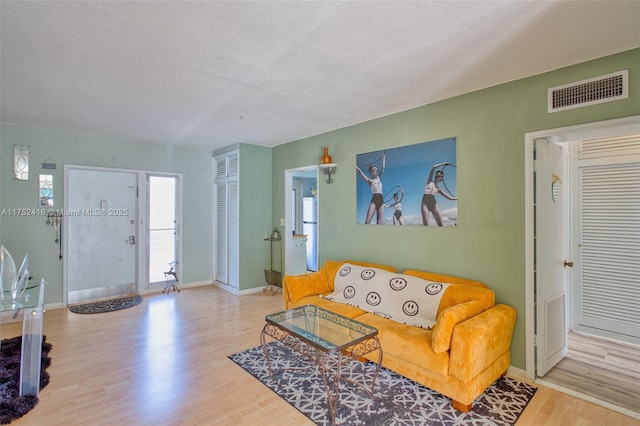 living room with baseboards, a textured ceiling, visible vents, and wood finished floors