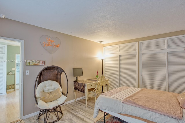 bedroom with light wood-type flooring, baseboards, visible vents, and a textured ceiling