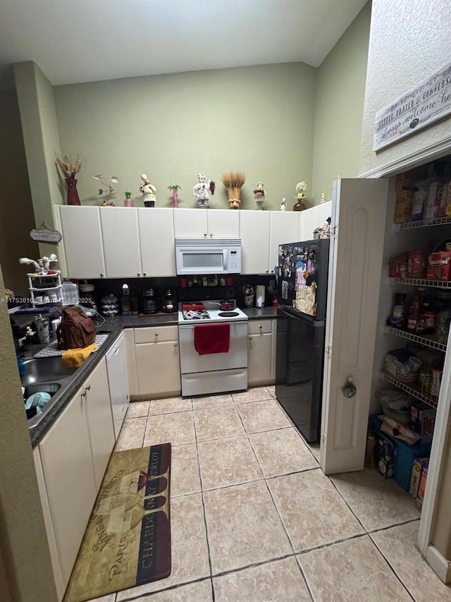 kitchen featuring light tile patterned floors, white appliances, dark countertops, and white cabinetry