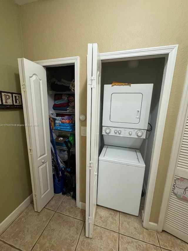 laundry area with laundry area, light tile patterned floors, baseboards, and stacked washer / drying machine