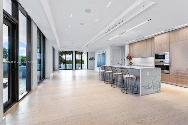 kitchen with a kitchen bar, double oven, modern cabinets, and light wood finished floors