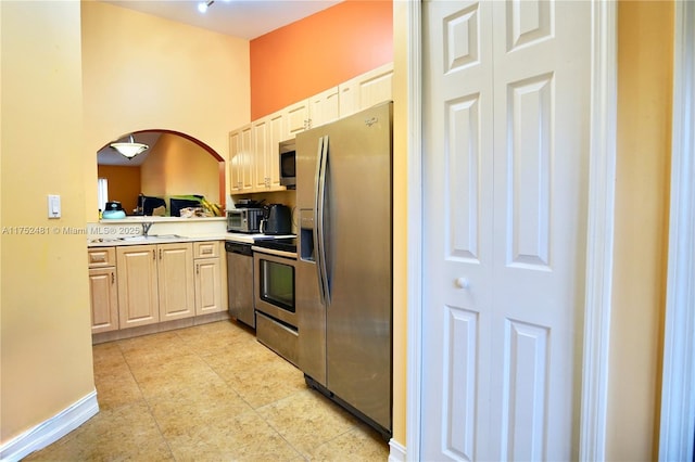 kitchen with arched walkways, light tile patterned floors, stainless steel appliances, light countertops, and a sink