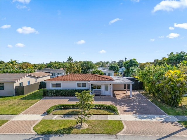 view of front of property featuring a tile roof, fence, decorative driveway, stucco siding, and a front lawn