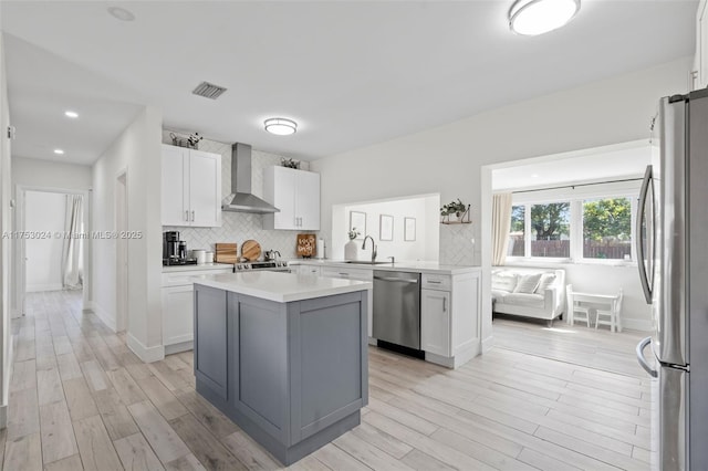 kitchen with stainless steel appliances, visible vents, decorative backsplash, a sink, and wall chimney range hood